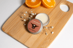 Balm tin labeled 'Citrus Dream' on a wooden board with oranges and flowers.