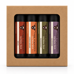 A set of four Tag Organics lip balm sticks in a kraft paper gift box. The lip balms are in flavors: Brieche, Citrus Dream, Peppermint, and Lavender, each with a distinct colored label (red-brown, orange, olive green, and purple) set against black tubes.