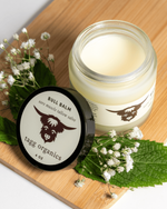 Jar of balm and its container on a wooden board with flowers and leaves