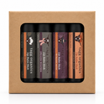 A boxed set of four lip balm tubes visible through a clear window in a kraft paper gift box. The labels read Tags Organics Lip Balm Size: Puppy Kick, Cowhide Kick, Swaffler Whiskers, and Pumpkin Patch.