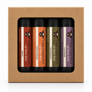 A set of four Tag Organics lip balm sticks in a kraft paper gift box. The lip balms are in flavors: Brieche, Citrus Dream, Peppermint, and Lavender, each with a distinct colored label (red-brown, orange, olive green, and purple) set against black tubes.