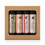 A boxed set of four lip balm sticks from Tags Organics, displayed in a brown kraft paper box with a clear window. The lip balms have black tubes with colorful labels in olive green, peach, pink, and cream.