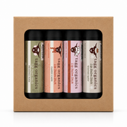A boxed set of four lip balm sticks from Tags Organics, displayed in a brown kraft paper box with a clear window. The lip balms have black tubes with colorful labels in olive green, peach, pink, and cream.