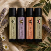 Four lip balm sticks from tags organics arranged on a wooden tray with a burlap cloth, lavender sprigs, and olive leaves around them. The labels show different scent colors: green, lavender, peach, and sage green.