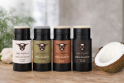Four bottles of tagg organics tallow deodorant on a wooden surface with a coconut in the background.