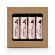 Four lip balm sticks in a kraft paper gift box, labeled 'tate organics lip balm stick VANILIA' with black caps visible through a front window.