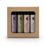 A set of four lip balm sticks in a kraft paper gift box. The lip balms are from the brand Tags Organics and include lavender, peppermint, vanilla, and unscented variants with different colored labels.
